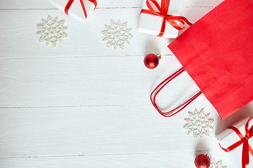 Top view Christmas red paper bag with gifts and snowflakes on white wooden background. Christmas shopping concept, Space for text, Holiday card