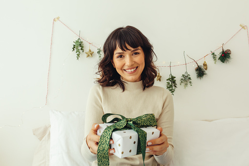 Close up of happy woman holding a Christmas present. Woman celebrating Christmas at home.