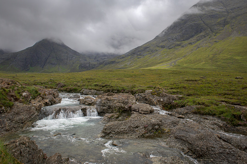 Rocks on the banks of a waterfall in front of The Cuillins close to the Fairy Pools near Glen Brittle on the Isle of Skye in Scotland.