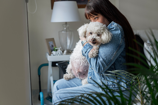 Latina owner from Bogotá Colombia between 40 and 44 years old, with her old breed of French poodle she has him hugged because of his great fatness and difficulty walking through the window.