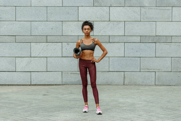 istock Pretty slim sportswoman holds mat standing by stone wall 1347681053