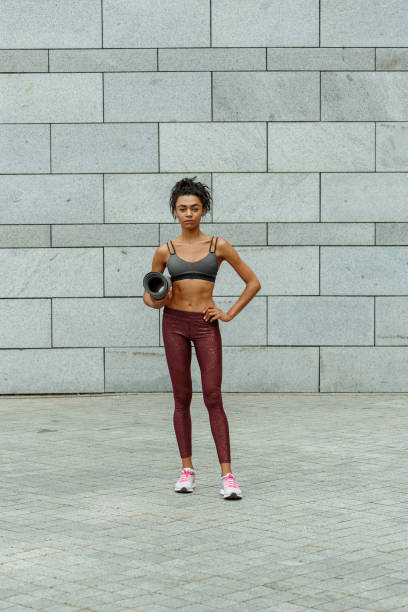 istock Pretty slim sportswoman holds mat standing by stone wall 1347681055