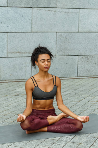 istock Positive lady meditates in lotus pose on mat by stone wall 1347681123