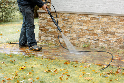 Man cleaning street with high pressure power washer, washing stone garden paths. High quality photo