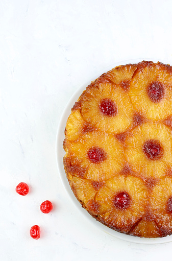Homemade pineapple upside down cake with glacé cherry on white background. Directly above.