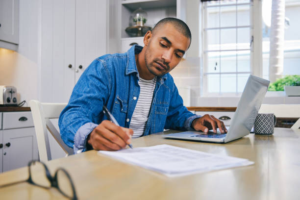 istock Shot of a young man using a laptop and going through paperwork at home 1347682313