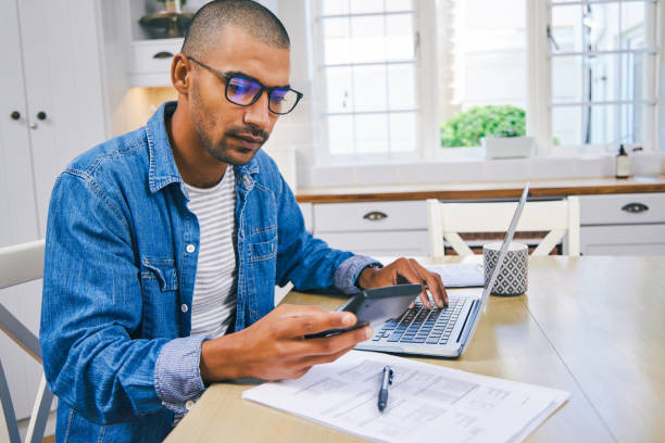 istock Shot of a young man using a laptop and going through paperwork at home 1347682316