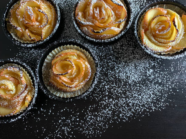 Homemade puff pastry apple roses sprinkled with sugar on dark background. Baked apple roses. Directly above.