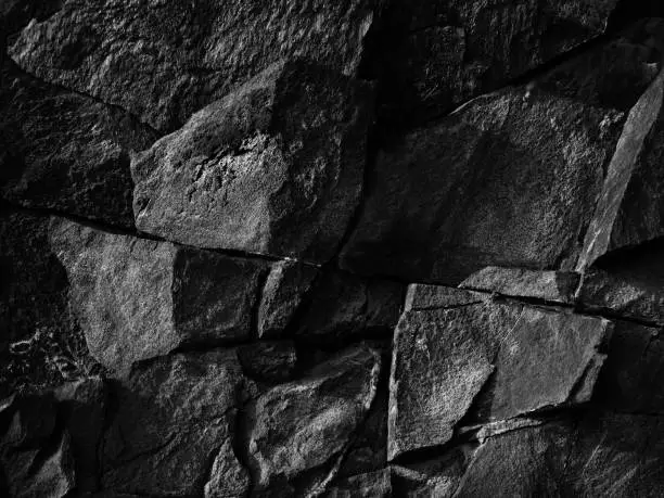 Destroyed cracked mountain surface. Close-up. It looks like a stone wall. Black grunge background with copy space for design.