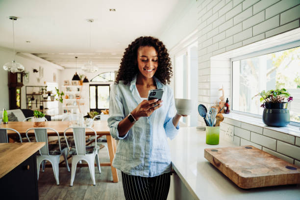 istock Woman chatting on cellphone standing in kitchen with coffee mug 1347694677