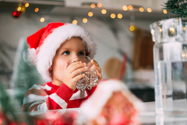 Cute boy kid in a red Santa hat drinking filtered water from a glass in the kitchen. Holidays, health concept. Cute boy kid in a red Santa hat drinking filtered water from a glass in the kitchen. Holidays, health concept purified water photos stock pictures, royalty-free photos & images
