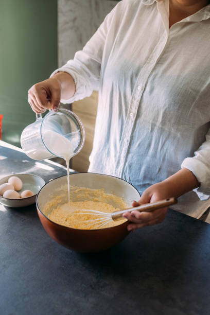istock Unrecognizable Plus Size Female Pastry Chef Making Bread in a Domestic Kitchen, Adding Milk to the Dough 1347703422