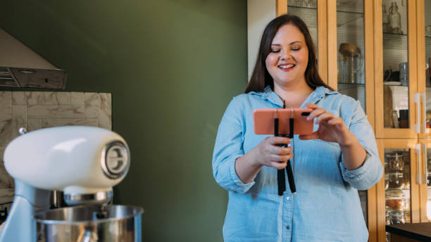 istock Smiling Overweight Female Baker Setting up her Smartphone on a Tripod Stand while Baking in a Domestic Kitchen 1347703455