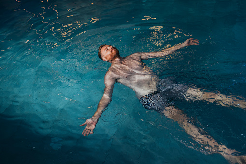 Handsome man in swimwear floating in the pool