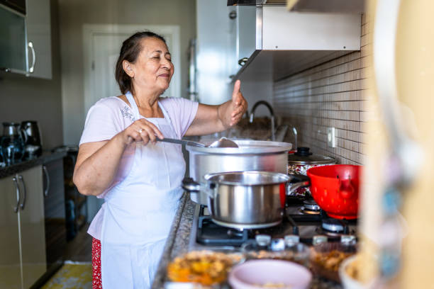 Elderly woman is cooking for the whole family in the kitchen and smelling the food Elderly woman is cooking for the whole family in the kitchen and smelling the food community center food stock pictures, royalty-free photos & images