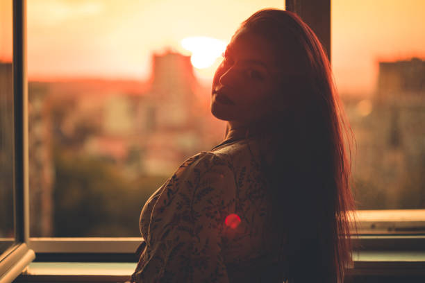 istock Beautiful woman standing at window at sunset 1347706307