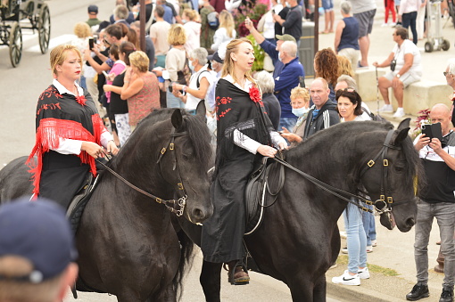 Saintes Maries, France - Septembre 25, 2021: Equine Festival in the streets of the city with parades, exhibitions and sale of horses and accessories. men and women on horseback cross the streets of the city with a crowd of people on either side of the street