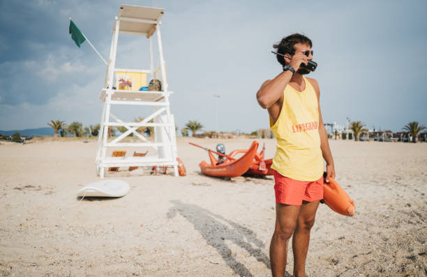 sauveteur utilisant son walky talky, radio - shorts rear view summer beach photos et images de collection