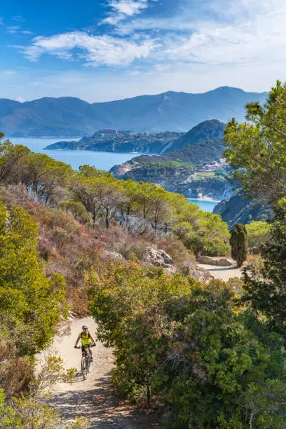 nice woman riding her electric mountain bike on the coastline above the mediterranean sea on the Island of Elba in the tuscan Archipelago, Tuscany, Italy