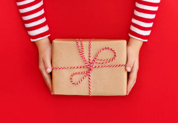 istock gift box in children's hands on a red background, presenting a gift, christmas background 1347715194