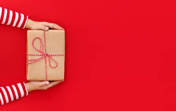 istock gift box in children's hands on a red background, presenting a gift, christmas background 1347715233