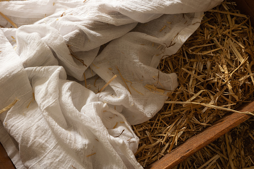 Wood manger or cradle with hay or straw and white linen swaddling cloth close up from above with copy space