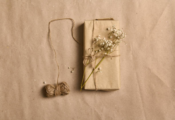 istock Flat lay spring composition with white gypsophila sprig on gift box in kraft wrapping paper and tied rope bow on crumpled cardboard background with copy space for advertisement 1347717710