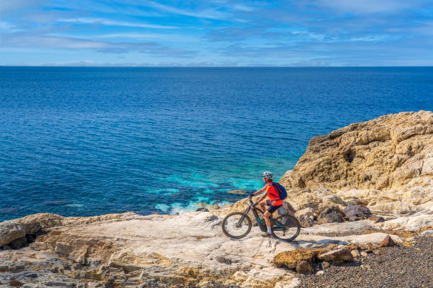 woman on electric mountainbike at the coastline of Elba Island, Tuscany, Italy nice woman riding her electric mountain bike on the coastline above the mediterranean sea on the Island of Elba in the tuscan Archipelago, Tuscany, Italy livorno stock pictures, royalty-free photos & images