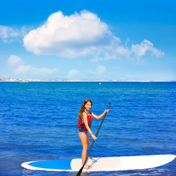 istock Kid paddle surf surfer girl with row in the beach 1347720390