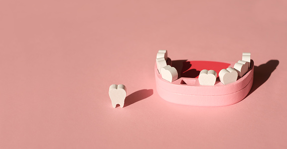 Wooden model toy of a human jaw with a missing tooth on a pink studio background. The problem of tooth loss. Baby milk teeth. Banner. Copy space.