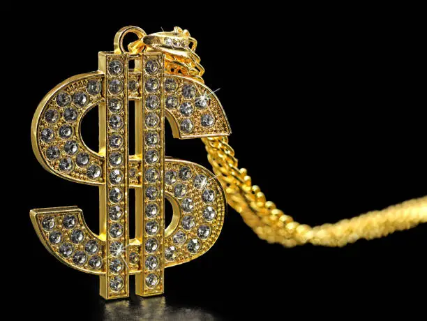 golden necklace dollar symbol with sparkling diamonds isolated on black background, close up.