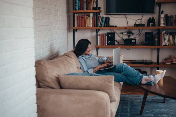 istock Young beautiful woman using a laptop while relaxing on the couch at home 1347725010