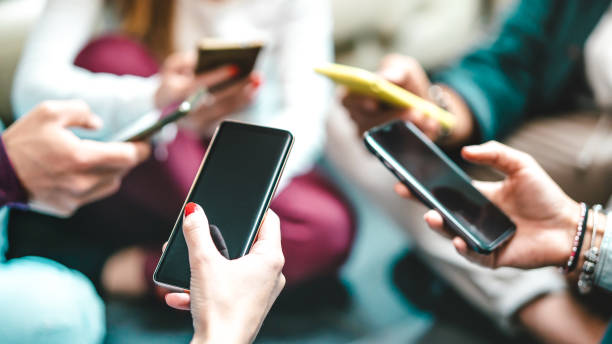 closeup of blogger hands using data on mobile smartphones - detail of friends sharing images on social media with smart phones - tech and cellphone culture concept with selective focus on left thumb - generation gap imagens e fotografias de stock