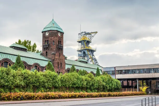 Historical buildings of the coal mine 'Wieczorek' in Katowice, Silesia, Poland. Old, brick, industrial building and mine shaft tower on a cloudy day.