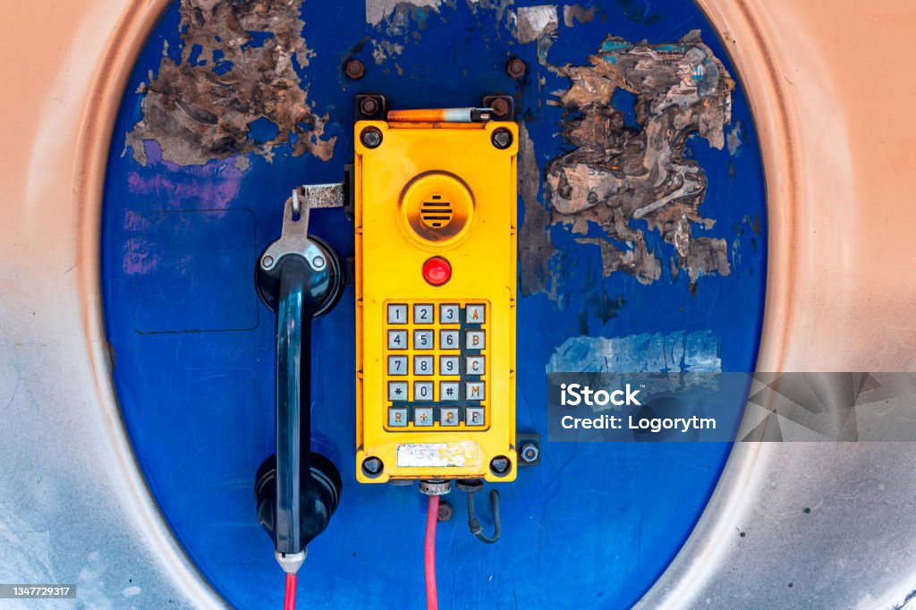 Old, rusted blue telephone booth with old yellow phone inside. City Street Stock Photo