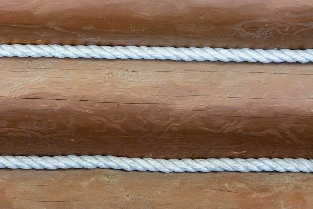 Wall of brown painted logs decorated with white braided ropes for use as abstract backgrounds and textures.
