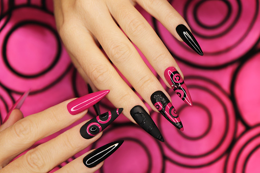 Fashionable pink and black manicure on long sharp nails.
