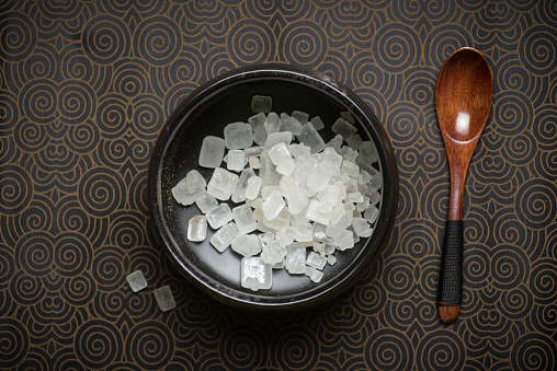 Chinese healthy white sugar in crystals in a black bowl on a black background