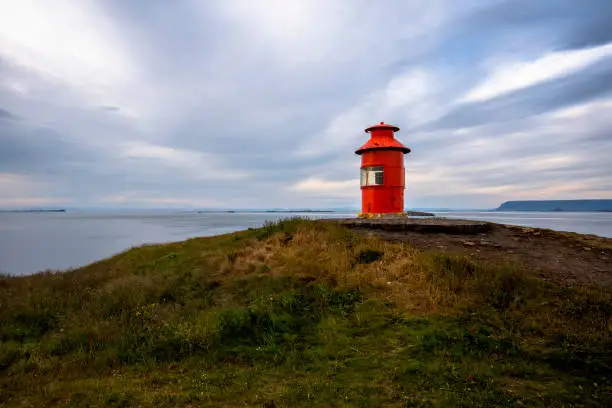 red lighthouse atop the headland of the Sugandisey Peninsula on Stikkysholmur Harbor in West Iceland