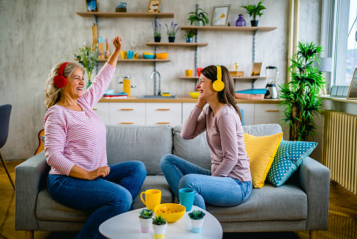 Mother and daughter having fun at home, listening music over headphones