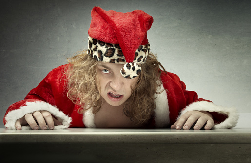 Grumpy man in Santa Claus costume sitting at the table against grungy background