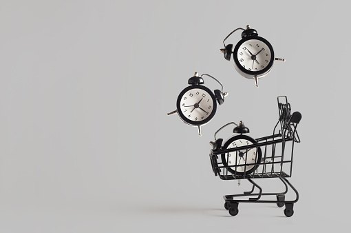 Toy shopping cart with three levitating alarm clocks on gray background with copy space. Black Friday banner, shopping concept. Sale idea.