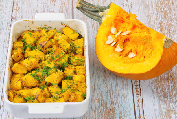 Roasted pumpkin in a ceramic pot on table with half raw squash close up