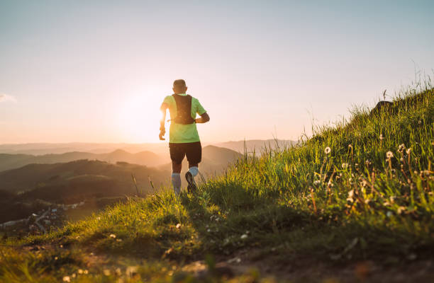 istock Active mountain trail runner dressed bright t-shirt with backpack running endurance marathon race by picturesque hills at sunset time back view photo. Sporty active people backlight concept image. 1347767730