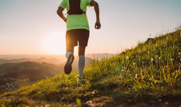 istock Active mountain trail runner dressed bright t-shirt with backpack running endurance marathon race by picturesque hills at sunset time back view photo. Sporty active people backlight concept image. 1347767731