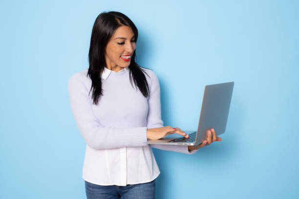istock Image of cheerful young woman standing isolated over blue background using laptop computer. 1347770155