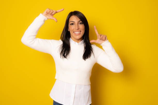 istock Happy woman making frame with fingers isolated on a yellow background 1347771488