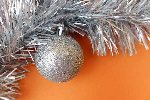 istock silver shiny Christmas ball with silver tinsel on an orange background. Festive background 1347774762
