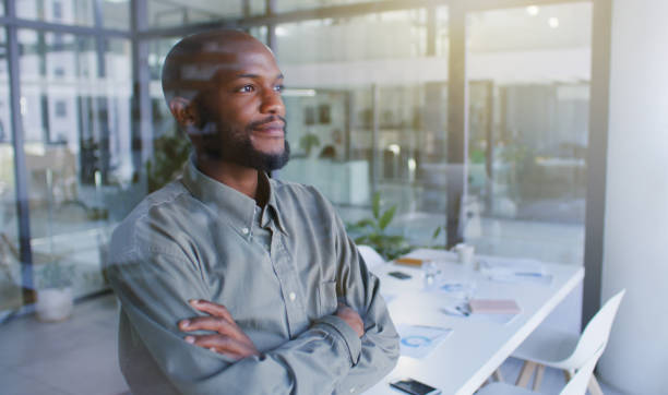 shot of a confident young businessman looking thoughtfully out of a window in a modern office - staring imagens e fotografias de stock