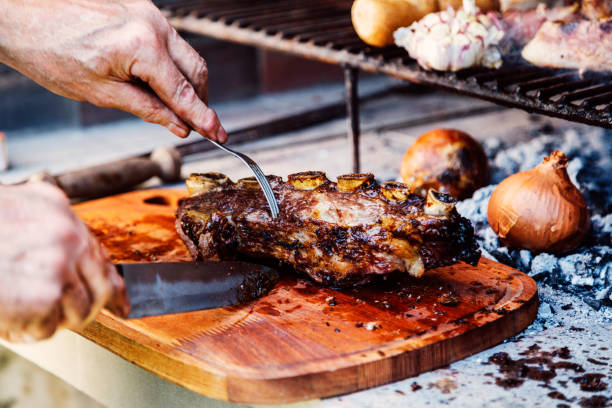 uomo argentino che taglia le costolette di roast beef. asado tradizionale dall'argentina. barbecue. - argentino ethnicity foto e immagini stock